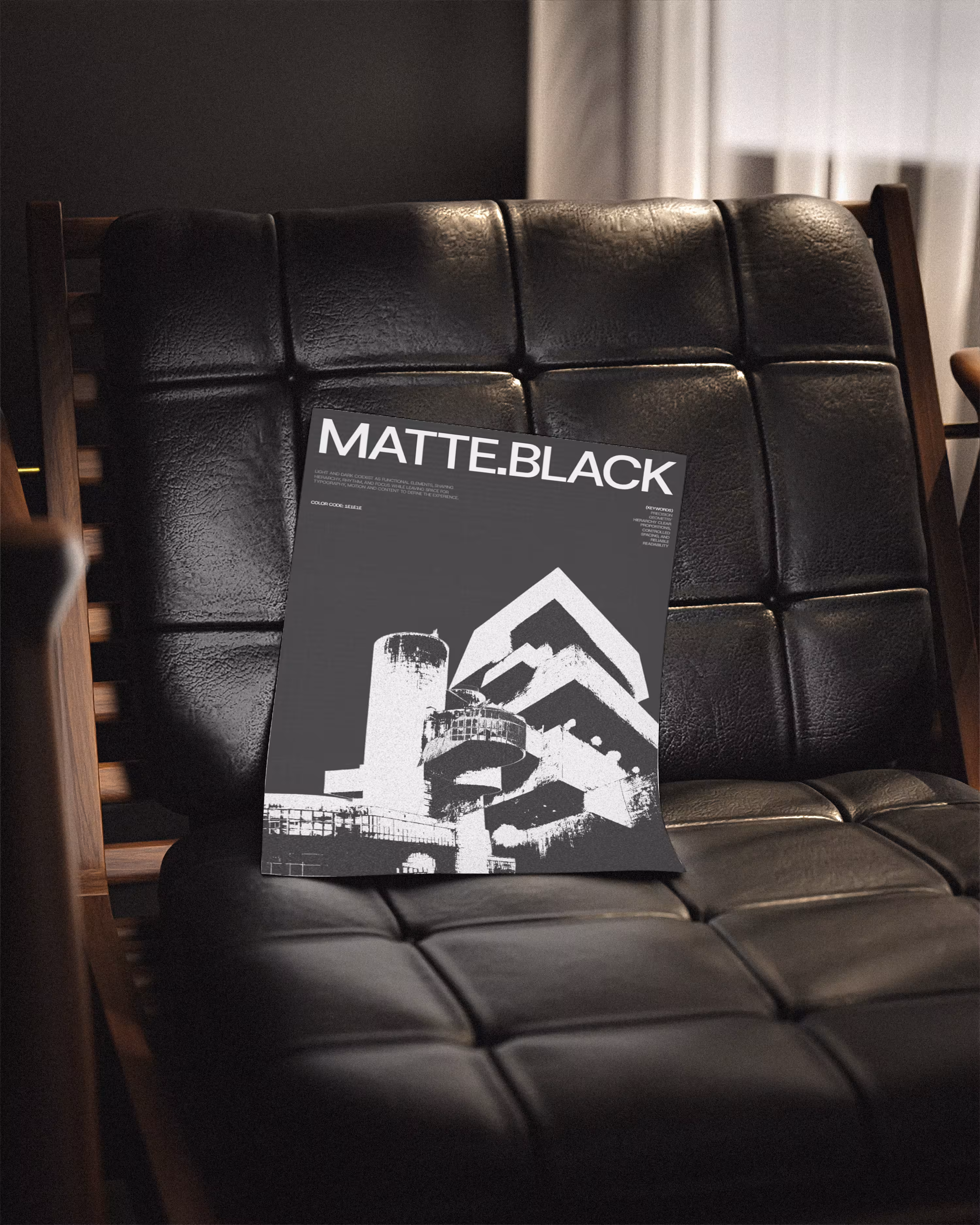 Black and white poster with modern architecture titled 'MATTE.BLACK' placed on a black leather chair.